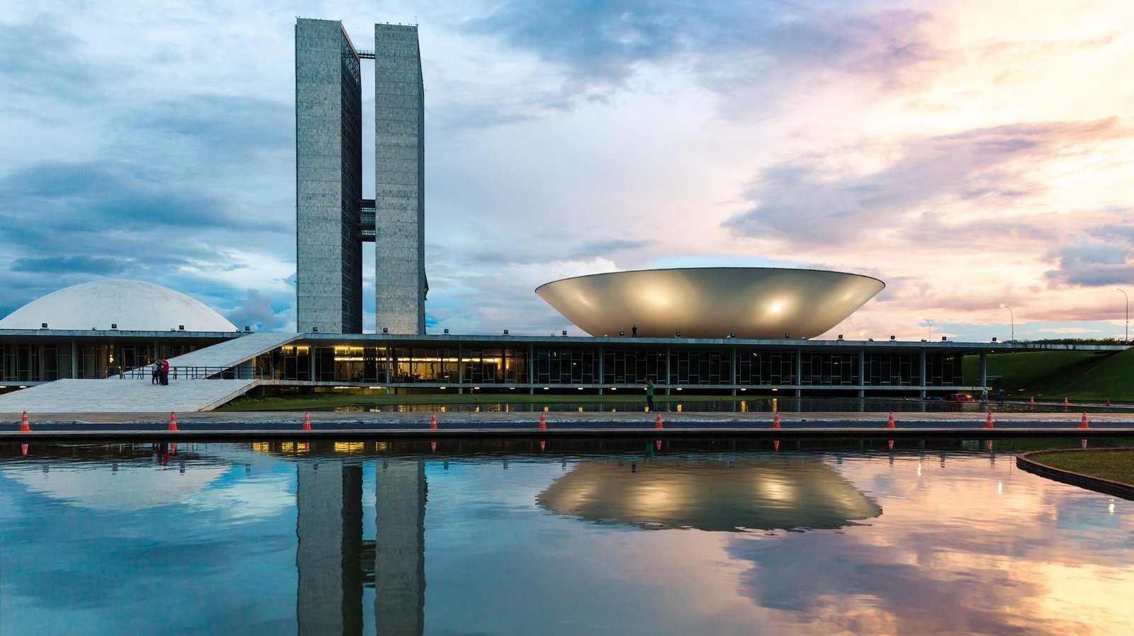 A modern, abstract architectural detail or cityscape representing Brasília, Brazil. High-contrast, vibrant, with subtle neon lighting accents against a bright sky to maintain the energetic, modern travel aesthetic. The image serves as an engaging backdrop.