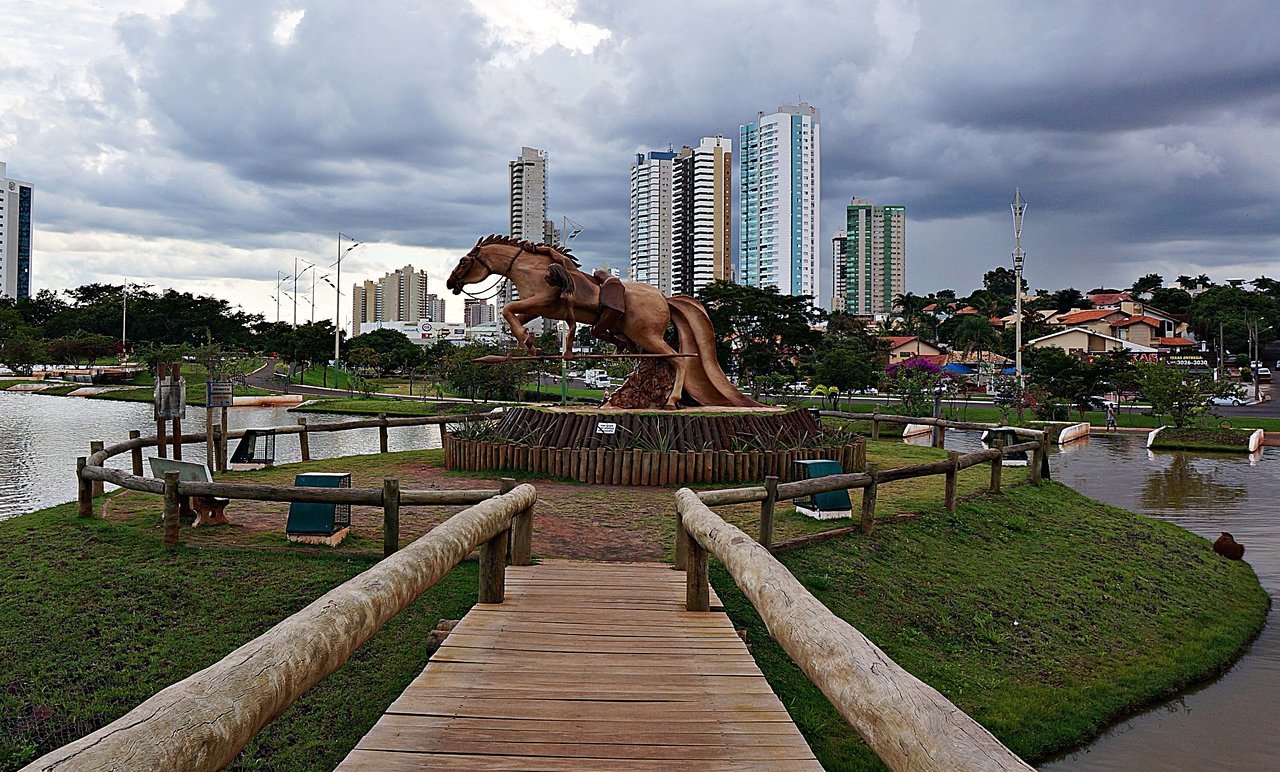 A modern, abstract architectural detail or cityscape representing Campo Grande, Brazil. High-contrast, vibrant, with subtle neon lighting accents against a bright sky to maintain the energetic, modern travel aesthetic. The image serves as an engaging backdrop.