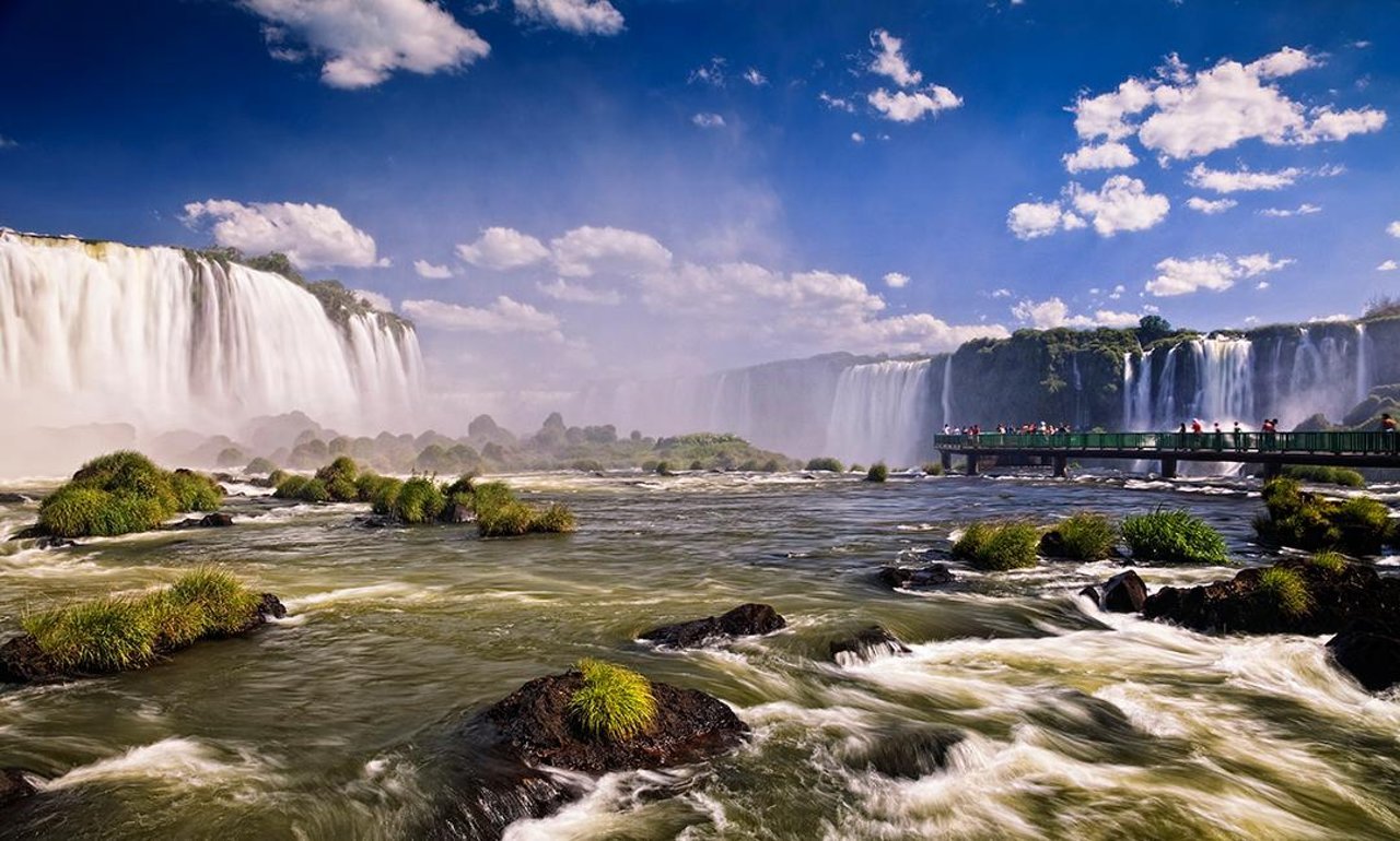 A modern, abstract architectural detail or cityscape representing Foz do Iguaçu and Cascavel, Brazil. High-contrast, vibrant, with subtle neon lighting accents against a bright sky to maintain the energetic, modern travel aesthetic. The image serves as an engaging backdrop.