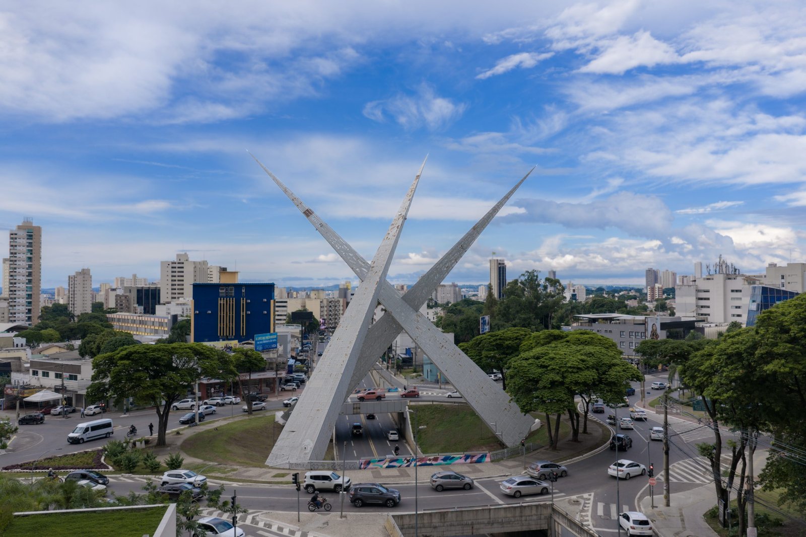 A modern, abstract architectural detail or cityscape representing Goiânia, Brazil. High-contrast, vibrant, with subtle neon lighting accents against a bright sky to maintain the energetic, modern travel aesthetic. The image serves as an engaging backdrop.